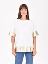 Remera blanca de corte holgado con mangas cortas y estampado dorado en el frente y en los bordes.