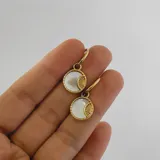 Par de aros dorados de acero quirúrgico hipoalergénico con baño en oro 18K y dije circular con incrustación de nácar y diseño de rayos de sol.