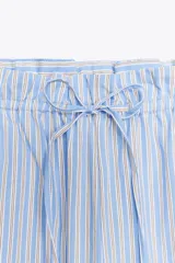 Pantalón tipo barrel con rayas verticales celestes y blancas, tiro medio y cintura elástica ajustable con lazo. Tiene bolsillos laterales y falsos bolsillos de vivo en la espalda.