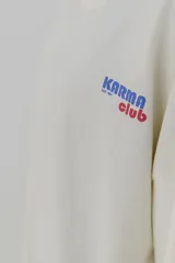 Remera gris de corte oversize con cuello redondo y estampado pequeño en el pecho con la frase "Karma Club" en color lila.