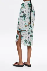 Vestido camisero corto de corte oversize, color blanco con bordado floral. Tiene cierre con botonadura frontal, escote camisero, manga larga con forma suave y puño, y bolsillo plastrón en el pecho.