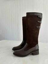 Bota alta de cuero negro con caña alta y taco cuadrado. Presenta tres correas con hebillas plateadas en la parte superior de la caña. Fabricada en Colombia.