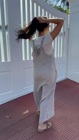 Mono largo de lino color beige, con breteles finos ajustables que se atan en la espalda, corte holgado y bolsillos laterales.