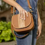 Bandolera de cuero color marrón con correa larga regulable, solapa con diseño trenzado y cierre con broche imantado.