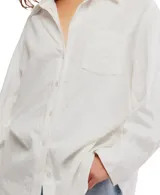 Camisa blanca de algodón con cuello clásico, manga larga y cierre frontal con botones. Tiene un bolsillo en el pecho y corte ligeramente entallado.