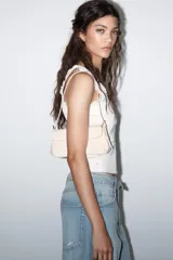 Bolso de hombro color crema con efecto acharolado, solapa con cierre magnético y asa ajustable.