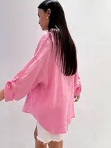 Camisa oversize rosada de lino, con cuello clásico, cierre frontal con botones, dos bolsillos de parche en el pecho y mangas largas con puños abotonados.