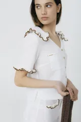 Blusa blanca de lino con cuello y mangas cortas con volados con borde de crochet marrón.