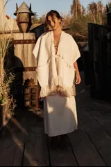 Ruana color crema con flecos y pompones.