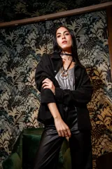 Chaqueta negra de gamuza con cuello camisero, cierre frontal con botones y bolsillos laterales.
