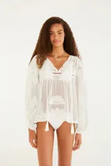 Blusa blanca con diseño cutwork, escote en V con cordones para anudar, mangas largas con leve frunce y puños ajustables.