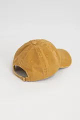 Gorro de gabardina color mostaza, estilo béisbol, con visera curva y orificios de ventilación bordados.