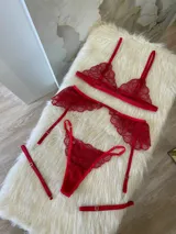 Conjunto de lencería rojo de encaje, compuesto por un bralette con breteles regulables, una tanga regulable con corte media less y un portaligas con volados.