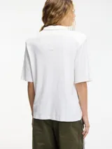 Remera tipo polo blanca de manga corta con hombreras y pins removibles en la delantera.