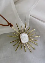 Collar con dije de bronce con forma de sol y centro de nácar, engarzado en un cordón de cuero marrón con detalles de bronce.