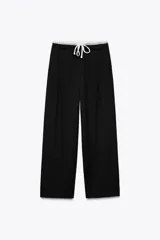 Pantalón negro de tiro alto con doble cintura elástica ajustable con cordón y tejido combinado. Pinzas frontales, bolsillos delanteros y falso bolsillo de vivo en espalda. Pernera ancha.