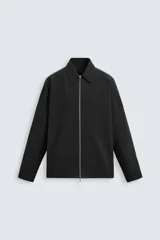 Sobrecamisa negra de corte recto, confeccionada en tejido técnico ligero, con cuello solapa, manga larga con puños abotonados, bajo ajustable con elástico en los laterales y cierre frontal con cremallera plateada.