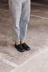 Mocasín de cuero negro con cordones y tachas metálicas en la puntera.