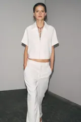 Chaqueta corta negra de cuello solapa y manga corta. Cierre frontal con cremallera metálica y bolsillos de ojal. Zara Woman Collection.