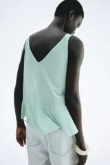 Musculosa de punto color verde menta, con escote en V adornado con volados que caen verticalmente por el centro. El bajo presenta un ruedo con doble capa de volados.