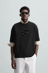 Camiseta negra de corte holgado, cuello redondo y manga corta. Estampado frontal con diseño abstracto en color blanco.