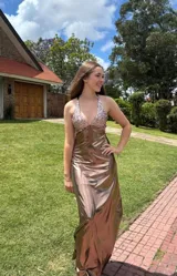 Vestido largo color marrón cobrizo con escote en V, cut outs laterales bajo el busto y breteles finos que se cruzan y atan en la espalda. Presenta un top con estampado abstracto en tonos marrones y dorados.