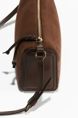 Cartera bandolera chica color marrón de gamuza, con cierre superior y correa ajustable.