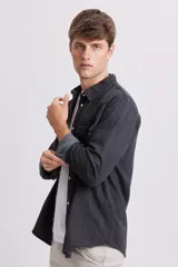 Camisa de jean de manga larga, color gris oscuro lavado, con cuello y botones a presión blancos. Presenta dos bolsillos frontales con solapa y pespuntes visibles.