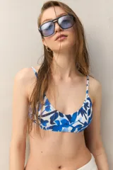 Top de bikini blanco con estampado de hojas azules, escote redondeado y tirantes finos.