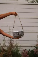 Bandolera plateada con textura arrugada, múltiples compartimentos internos y doble correa.