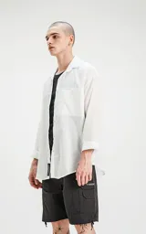 Camisa manga larga blanca de calce oversize con bolsillo con ojal y botón en delantero, confeccionada en textil plano fresco y liviano.