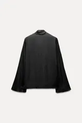 Blusa negra de cuello redondo con lazo en el mismo tejido. Manga larga acampanada y bajo recto.