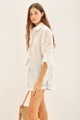 Camisa blanca de algodón con fit amplio, cuello y cartera frontal, y bordados calados en el frente, mangas y espalda. Posee tajos laterales y presillas internas para regular el largo de las mangas.