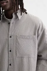 Camisa de hombre relaxed fit con cuello solapa, manga larga con puño abotonado, bolsillo de parche en el pecho y cierre frontal con botones. Diseño a cuadros en tonos gris y blanco.