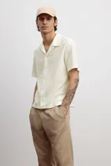 Camisa blanca de punto con textura acanalada, corte regular, cuello inglés, tapeta lisa, canesú en la espalda y bajo recto con aberturas laterales.