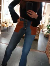 Pantalón de jean celeste con cintura elastizada, corte recto, bolsillos laterales y aplique de cuero marrón en el bolsillo delantero. Presenta botones metálicos en los laterales de la cintura y etiqueta de cuero en la parte trasera.