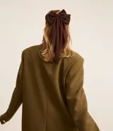 Accesorio para el pelo color marrón oscuro, con forma de lazo y caida de tejido. Modelo pinza.