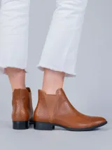 Bota tipo chelsea de cuero color marrón con textura grabada tipo reptil. Presenta paneles elásticos laterales a tono y suela de caucho termoplástico con tacón bajo.
