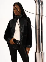 Chaqueta bomber negra con cuerpo de bouclé y mangas de cuero sintético. Presenta cuello mao, cierre frontal con cremallera, bolsillos con solapa y puños y bajo acanalados.