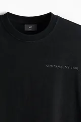 Remera negra de algodón con cuello redondo ribeteado acanalado, hombros caídos, diseño estampado con texto "New York, NY 11201" y bajo recto.
