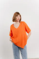 Blusa color naranja de lino, con escote en V, mangas cortas con vuelta y terminación asimétrica. Presenta una fila de botones decorativos en uno de los hombros.