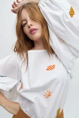 Blusa color arena de algodón con escote a la base y mangas abullonadas. Presenta bordados artesanales de motivos marinos en tonos naranja y azul.