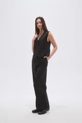 Chaleco negro con finas rayas verticales blancas (pinstripe), escote en V y cierre frontal de botones. Presenta bolsillos ribeteados en la parte inferior delantera.