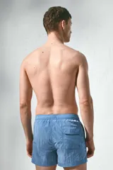 Short de baño azul de nylon con elástico revestido y cordón para ajustar oculto en la cintura, bolsillos laterales y bolsillo de solapa con cierre autoadherente atrás. Largo por encima de la rodilla con abertura corta en los laterales y suspensor interior en malla suave.