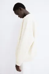 Buzo de tejido liso color crema, con cuello redondo acanalado, hombros caídos y puños y bajo acanalados.