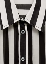 Camisa de manga larga con puños abotonados, cuello camisero y cierre frontal con botones. Diseño a rayas verticales blancas y negras sobre tejido semitransparente.