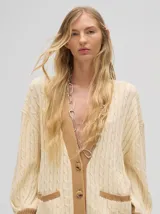 Cardigan largo color crema con detalles en color camel en el borde de los bolsillos, en el borde de los botones y en los puños. Tiene cuello en V y cierre con botones.