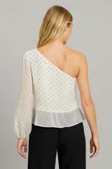 Blusa blanca asimétrica con un hombro descubierto, manga larga abullonada y estampado de lunares plateados.