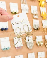 Aretes colgantes dorados con forma de flor estilizada, hechos de alambre metálico fino.