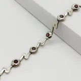 Pulsera de plata 925 con diseño ondulado y engastes circulares que contienen piedras granate redondas.